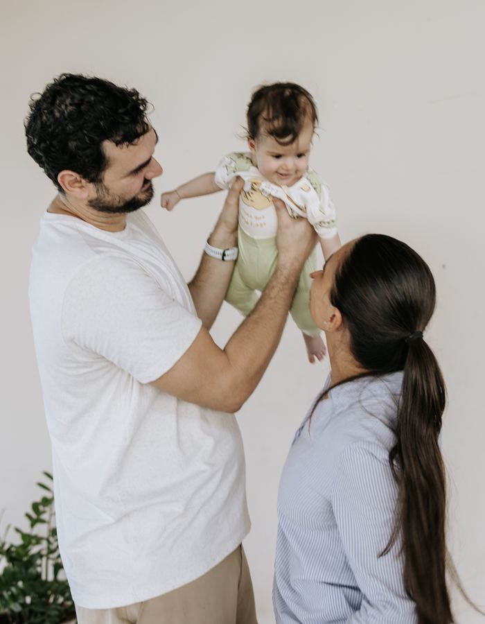 Pai levantando o bebê no colo, ao lado da mãe